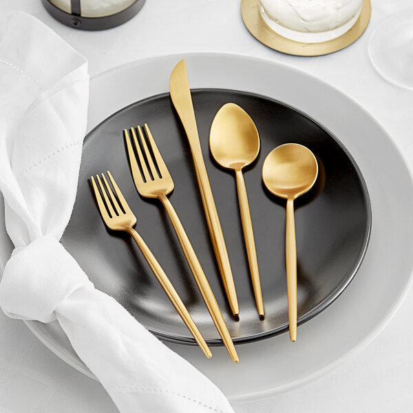 A five-piece set of gold brushed stainless steel flatware displayed on a black plate.