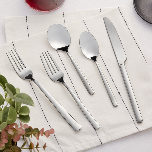 A five-piece set of stainless steel flatware including two forks, two spoons, and a knife, displayed on a white napkin.