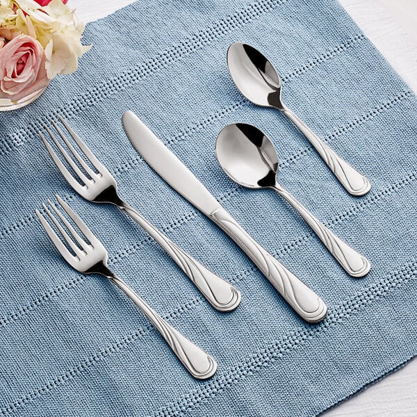 A five-piece set of Acopa Swirl 18/8 stainless steel extra heavy weight flatware displayed on a blue cloth.