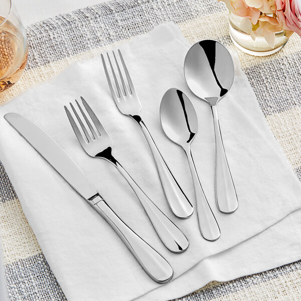 A five-piece set of stainless steel flatware including a knife, two forks, and two spoons, displayed on a white napkin.