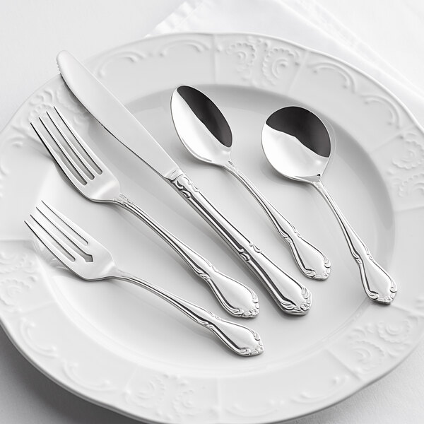 A five-piece set of stainless steel flatware with decorative handles, displayed on a white plate.