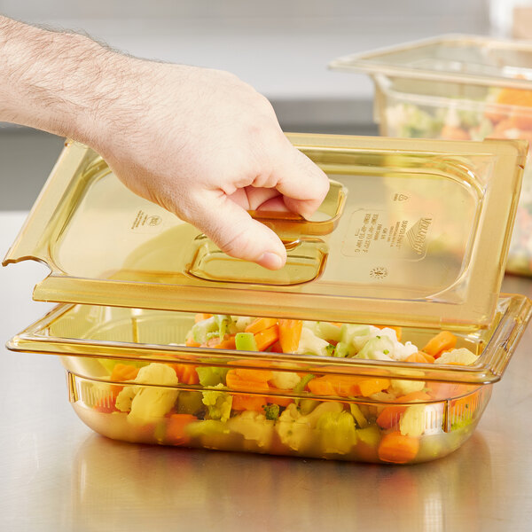 A hand holding a Vollrath amber high heat slotted lid over a container of food.