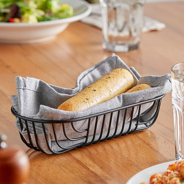 A black wire oval basket lined with a gray cloth, holding two breadsticks.
