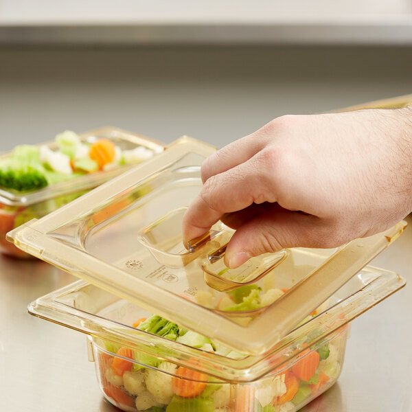 A person's hand pushing a Vollrath Super Pan high heat plastic lid onto a container of food.