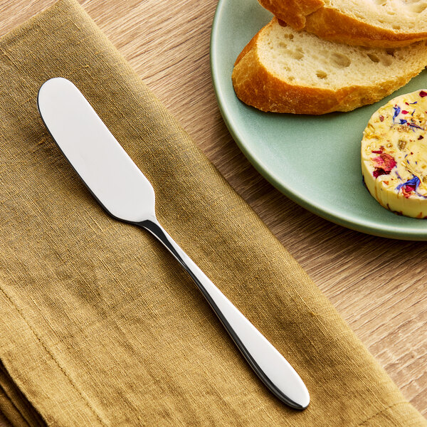 A stainless steel butter knife placed on a brown napkin next to a plate with bread and butter.