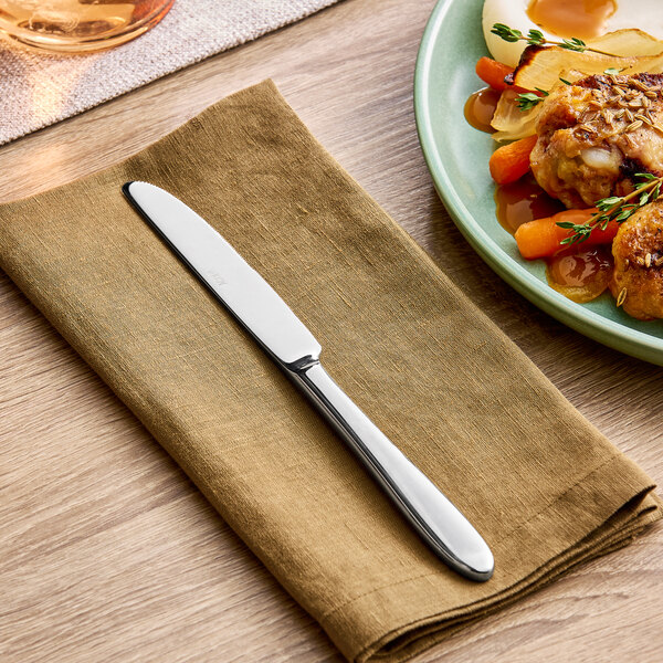 A stainless steel dinner knife placed on a brown napkin next to a plate of food.