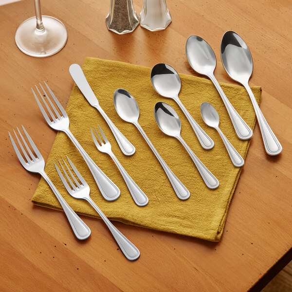 A set of stainless steel flatware including forks, spoons, and a knife arranged on a yellow napkin.