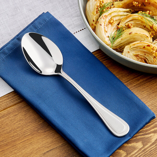 A stainless steel tablespoon or serving spoon with a simple, elegant handle design, placed on a blue napkin.
