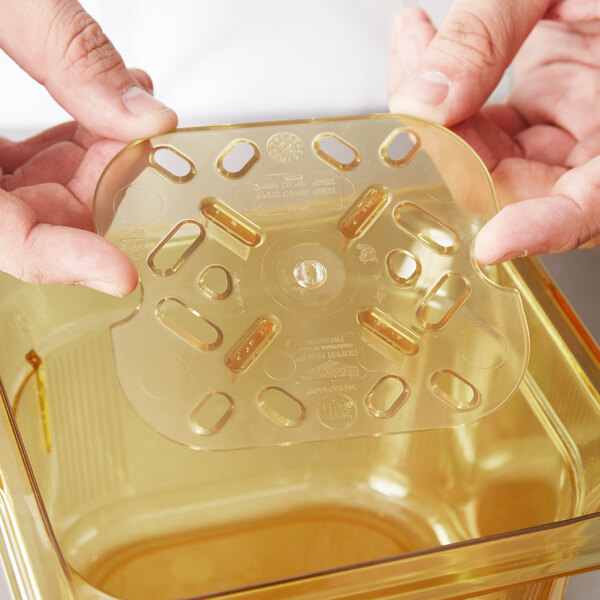 A person holding a Vollrath amber high heat plastic drain tray over a counter.