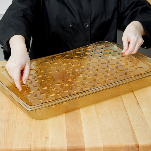 A woman in a chef's jacket holding a Vollrath amber high heat drain tray with honeycomb on a counter.