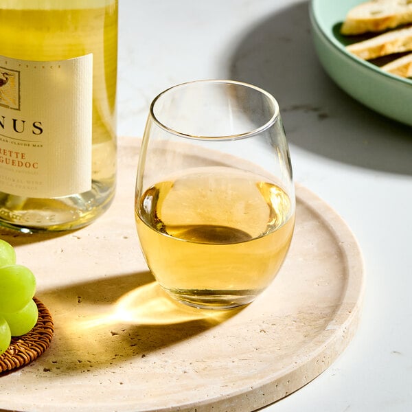 A clear 15 oz. stemless wine glass filled with white wine, placed on a round tray.