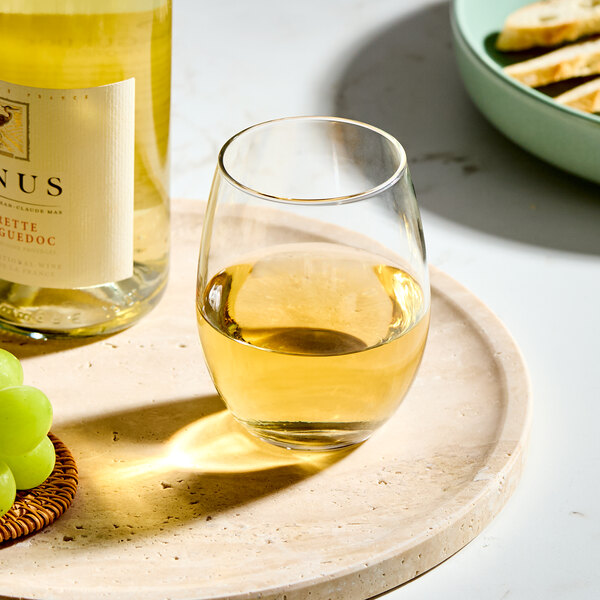 A clear, stemless wine glass filled with white wine, placed on a round tray.