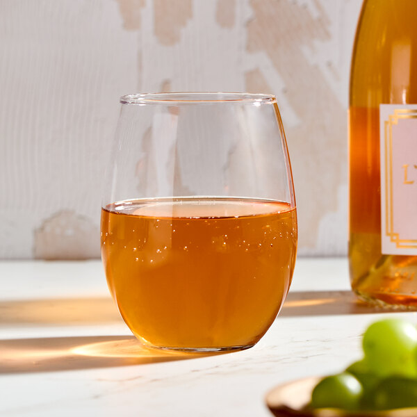A clear, stemless wine glass filled with a golden liquid, shown on a light surface.