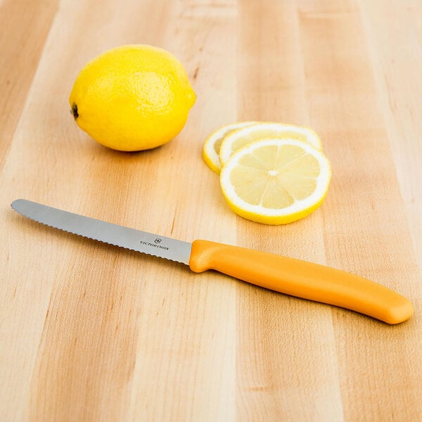 A Victorinox utility knife with a yellow handle cutting a lemon on a table.
