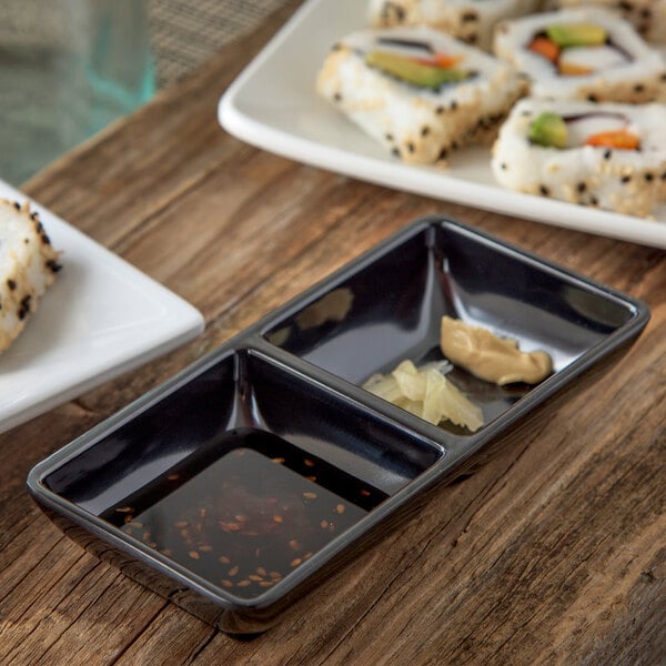 A rectangular black Carlisle ramekin with sushi and sauce on a wood surface.