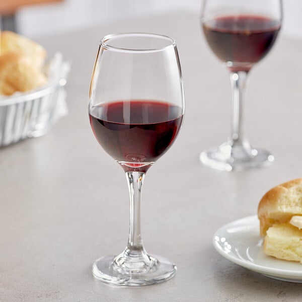 A close up of a glass of red wine next to a plate of bread.