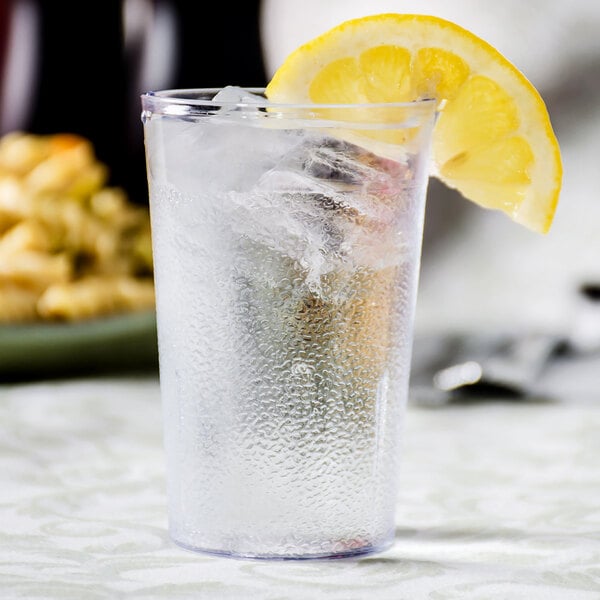 A Carlisle clear plastic tumbler filled with water and a lemon slice.