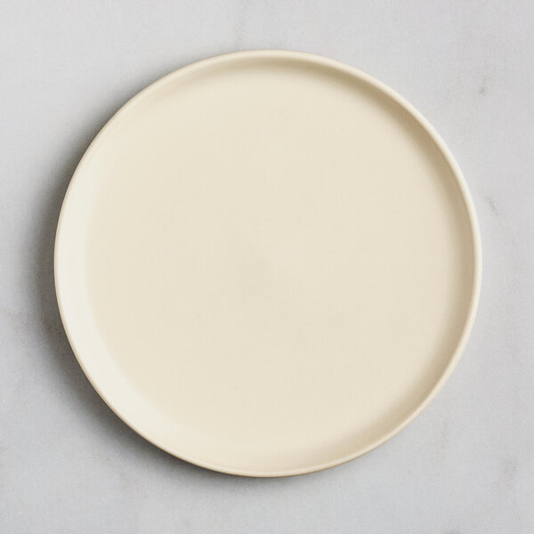 A round, matte, off-white plate with a slightly raised rim, shown from above on a light surface.