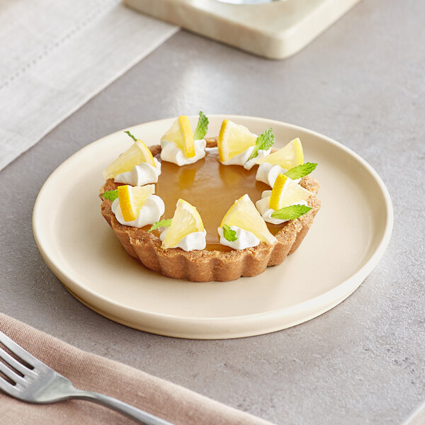 A small tart topped with whipped cream, lemon slices, and mint leaves is served on a round, off-white plate.