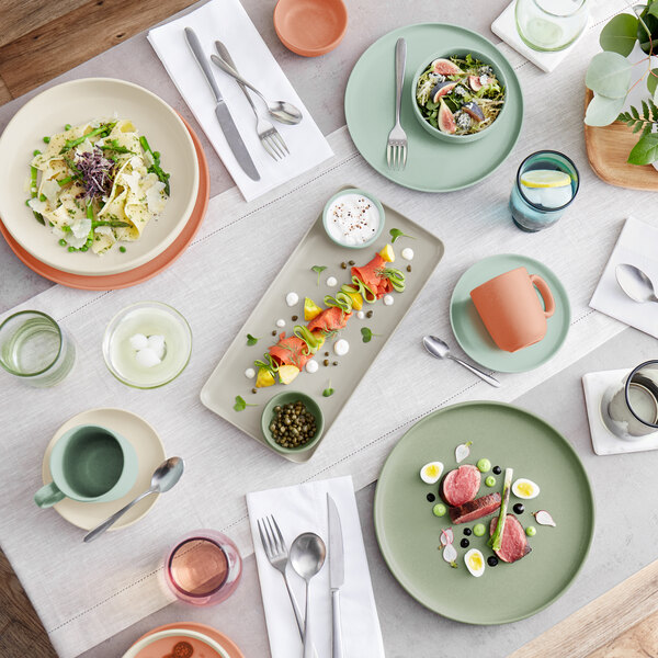 A table set with various pastel-colored plates, bowls, cups, and glasses, featuring a variety of plated dishes and drinks.