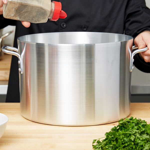 A chef pouring seasoning into a large silver Vollrath sauce pot.