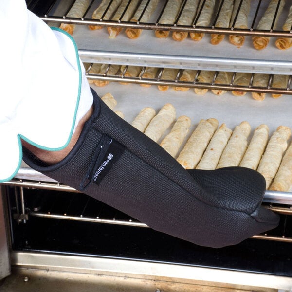 A person wearing a San Jamar black puppet style oven mitt taking pastries from a tray.