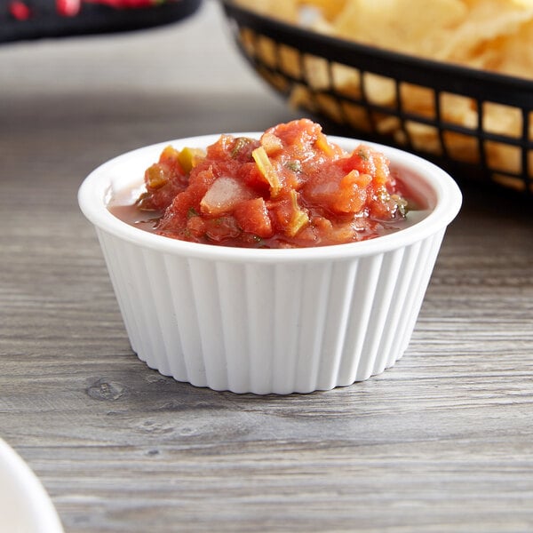 A white fluted Carlisle ramekin filled with salsa on a wood surface.