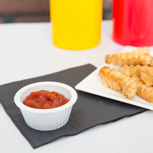 A white plate of french fries with a bowl of ketchup on a napkin.