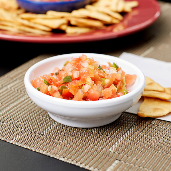 A white Carlisle salsa bowl filled with salsa and chips on a table.