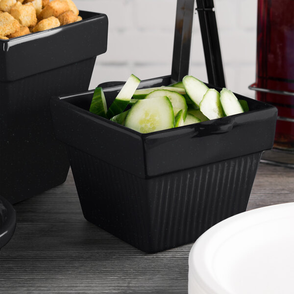 A black square Tablecraft condiment bowl with cucumbers and croutons.