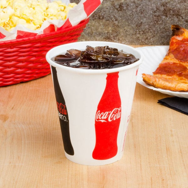 A Solo Coca-Cola paper cup filled with ice and soda on a counter with a bottle of soda and a basket of popcorn.
