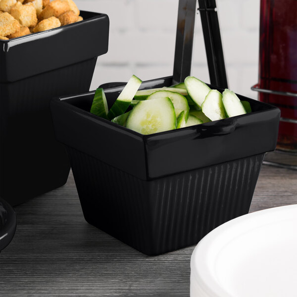 A black square Tablecraft condiment bowl with cucumbers in it.