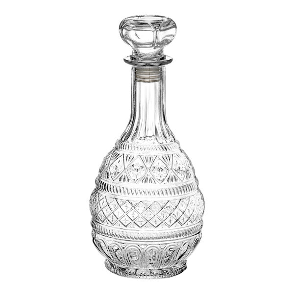 A clear, intricately cut glass decanter with a round stopper and decorative patterns.