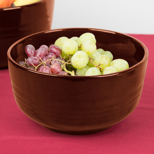 A Tablecraft copper cast aluminum fruit bowl filled with grapes on a table.