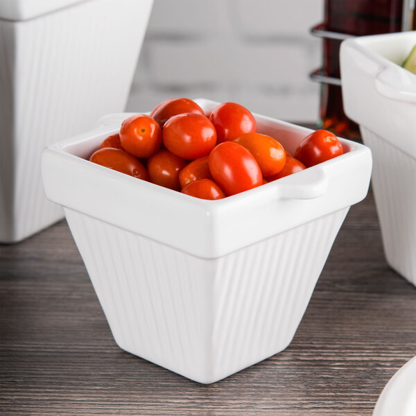A white Tablecraft square condiment bowl filled with cherry tomatoes.