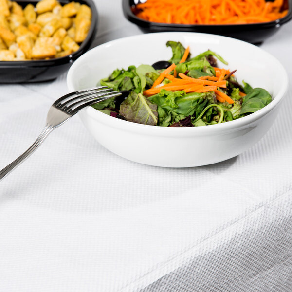 A bowl of salad with a fork on a table with a white table cover.