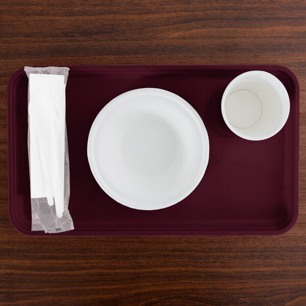 A rectangular burgundy Cambro tray with a white plate and a white cup on it.