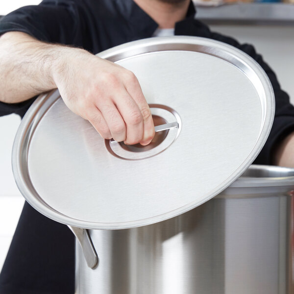 A person using a Vollrath stainless steel pot lid on a large pot.