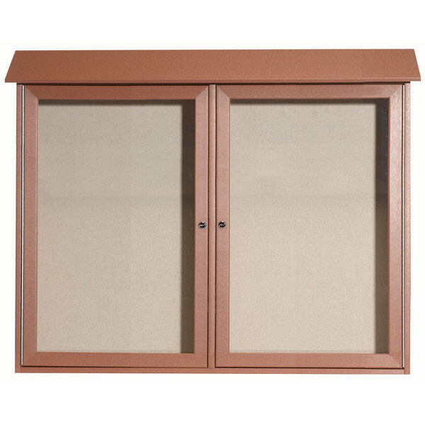 A brown cabinet with dual hinged glass doors enclosing two bulletin boards with vinyl tackboards.