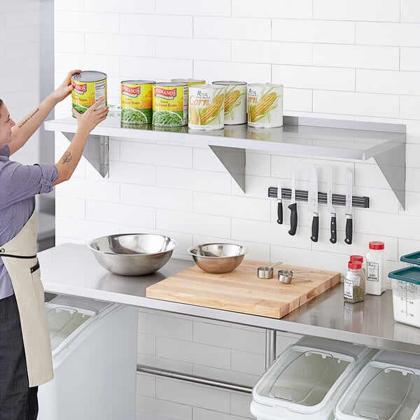 A woman in an apron putting a can on a Regency stainless steel wall shelf.