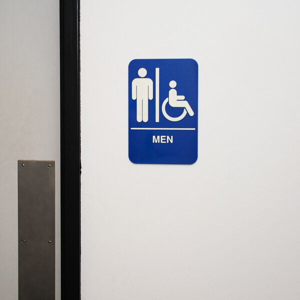 A blue and white rectangular metal sign with a man in a wheelchair and braille text that says "Men" on it.