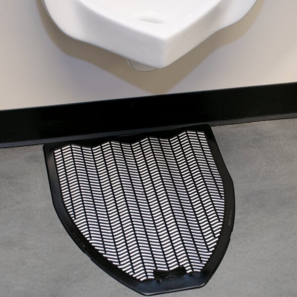 A black urinal mat on the floor next to a urinal.