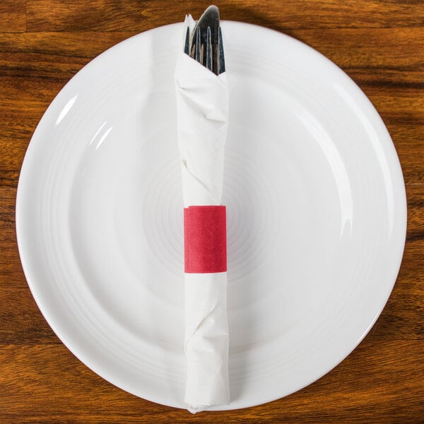 A red napkin wrapped around a fork and knife on a white plate.