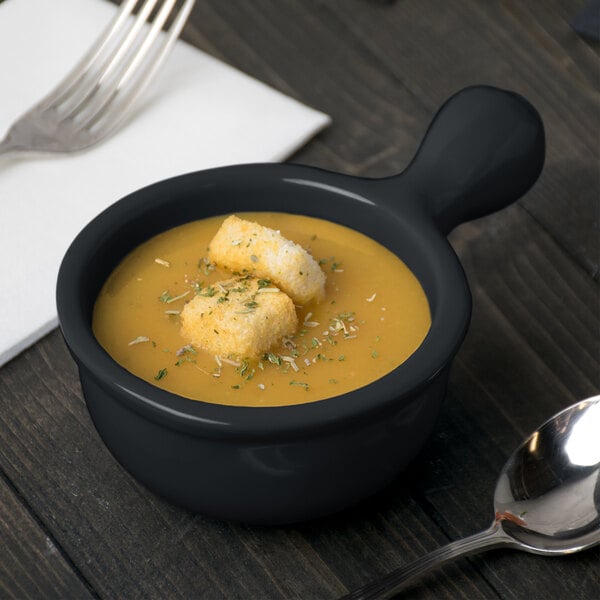 A black cast aluminum Tablecraft soup bowl with croutons and a fork.