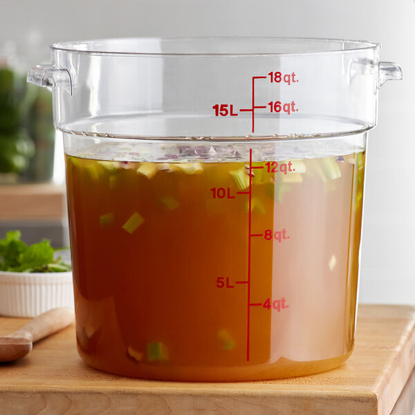 A Cambro clear round food storage container filled with brown liquid on a counter.