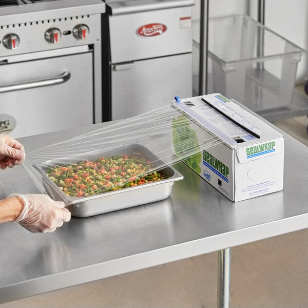 A person using Berry heavy-duty plastic wrap with a ZipSafe slide cutter to wrap a tray of vegetables.