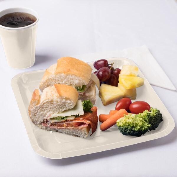 A sandwich on an ivory square paper plate with a cup of coffee.