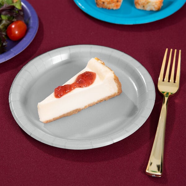 A slice of cheesecake with strawberry jam on a Creative Converting Shimmering Silver paper plate with a fork.
