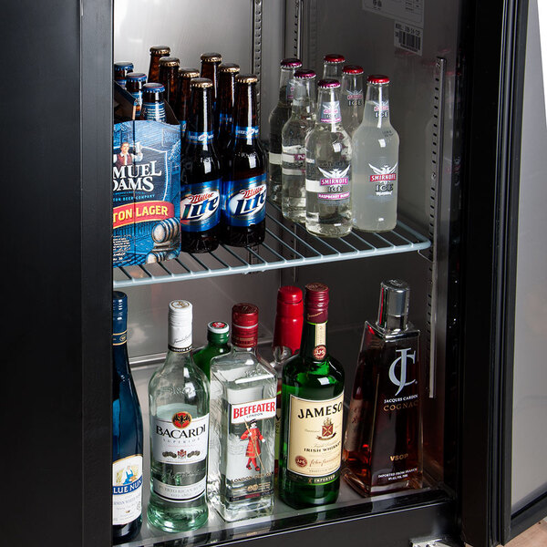 An Avantco back bar refrigerator shelf full of bottles of alcohol including a green and white labeled cognac bottle.