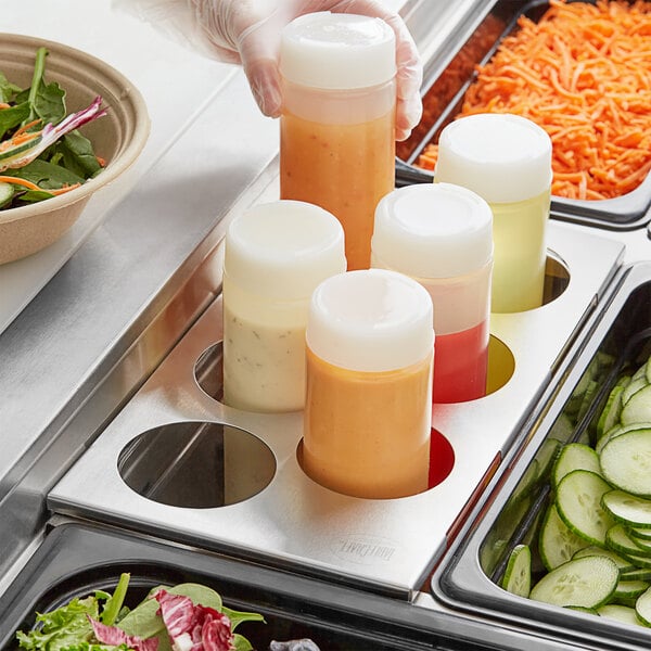 A Tablecraft six hole squeeze bottle holder on a counter in a salad bar filled with squeeze bottles of salad dressing.